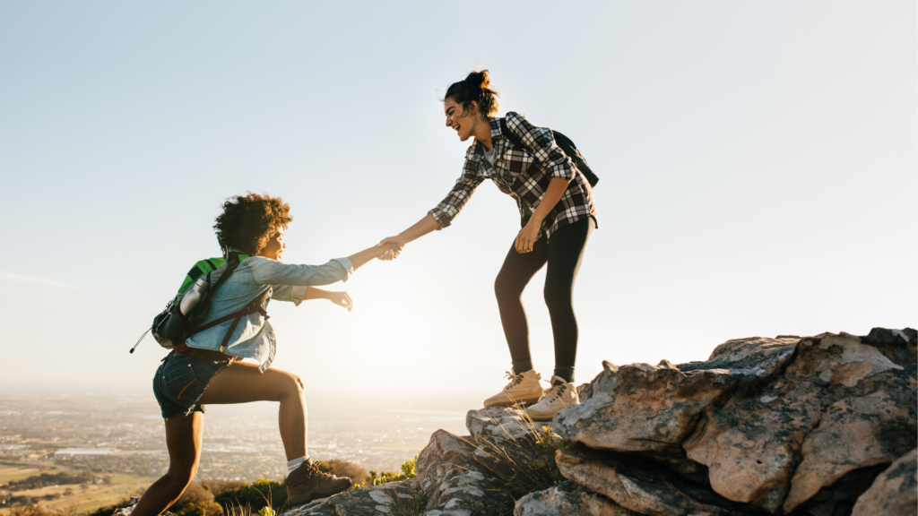 Two friends helping each other complete a hike.